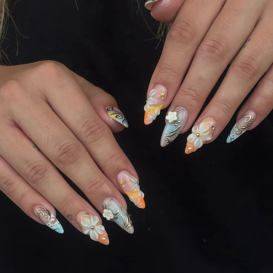 Lange Mandelnägel mit Farbverlauf in Pastellblau und Orange, weissen 3D-Blüten, goldenen Linien und Perlen